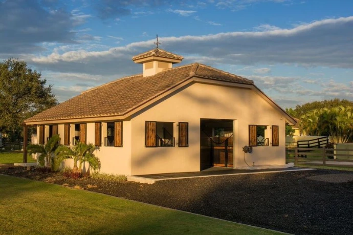 Mediterranean cream stucco barn with orange tile roof and cupola on green lawn