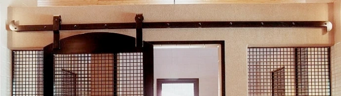 Decorative Flat Track: Interior barn aisle view showing mahogany sliding doors with wire mesh panels on decorative flat track hardware against cream colored walls